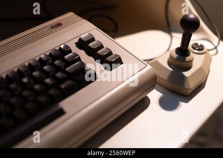 A retro computer and joystick placed on a desk indoors illuminated by warm light evoking nostalgic feelings of old technology Stock Photo