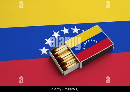 Venezuela flag is shown in an open matchbox, which is filled with matches and lies on a large flag. Stock Photo