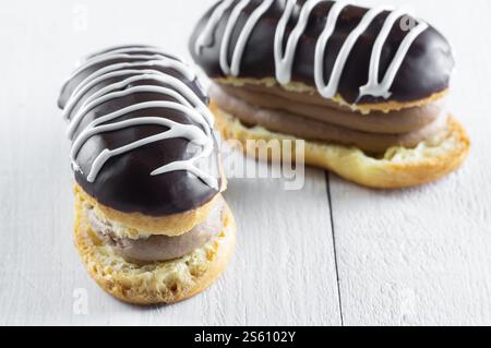 Eclairs with black chocolate and white chocolate with custard on rustic table. Traditional French dessert. Eclair Pastery concept Stock Photo