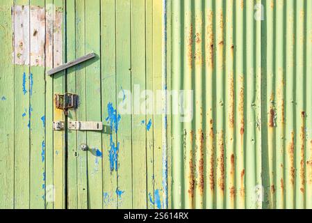 Vertical panels of green wood and corregated iron on an old wooden door with random paint and various locks texture and paint Stock Photo
