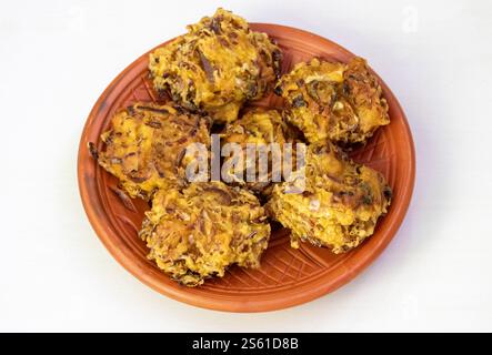 Crispy pakora on a clay plate, isolated on a white background. These delicious, deep-fried fritters are a popular snack or appetizer in Bangladesh, In Stock Photo