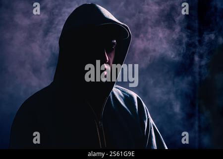 Criminal man in shadow. Scary suspicious gangster with hidden face and hoodie. Silhouette of stranger. Gang crime or stalker concept. Hooligan. Stock Photo
