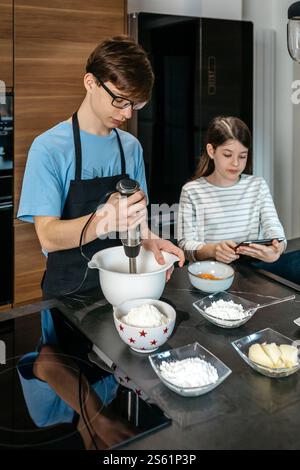 Teenagers preparing ingredients for baking a cake, using hand mixer and following online recipe Stock Photo