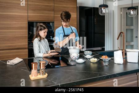 Teenagers preparing ingredients for baking a cake, using hand mixer and following online recipe Stock Photo