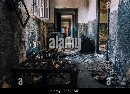 Abandoned corridor with charred debris, burnt walls, broken window frames, and scattered remnants inside ravaged building after catastrophic fire. Stock Photo