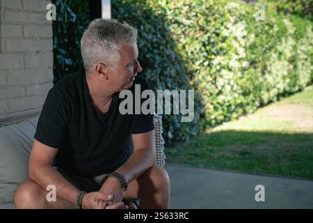 Mature man looking in profile and sitting comfortably on a couch in his backyard. Copy space. Stock Photo