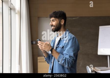 Smiling Arabian man office employee holding mobile phone at workplace Stock Photo