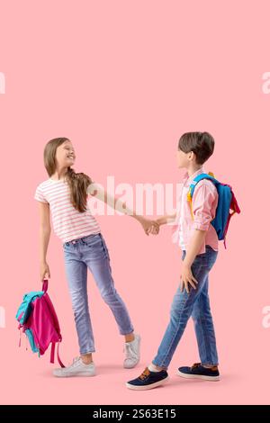 Little pupils with backpacks holding hands on pink background Stock Photo