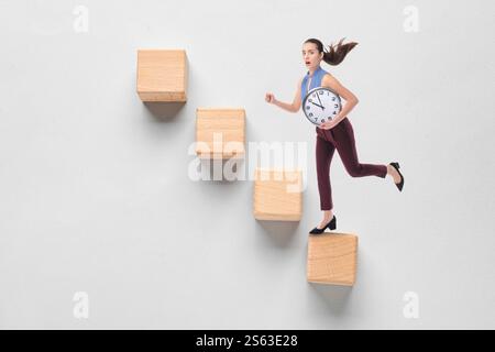Businesswoman with clock climbing career ladder on grey background Stock Photo