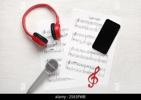 Modern mobile phone, music sheets, headphones and microphone on white wooden background Stock Photo