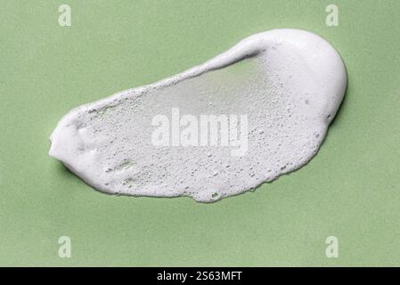 White face cleanser mousse texture swatch on olive green background. Gentle shampoo foam sample. Stock Photo