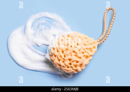 Sponge with white foam texture on blue background close up. Body care, dishware, cleaning and hygiene concept. Stock Photo