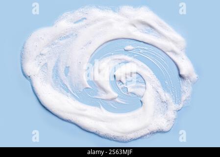 White soft foam texture sample on blue pastel background. Face cleanser mousse smudge, soap or shampoo foam. Cleaning, kitchenware, dishware concept t Stock Photo