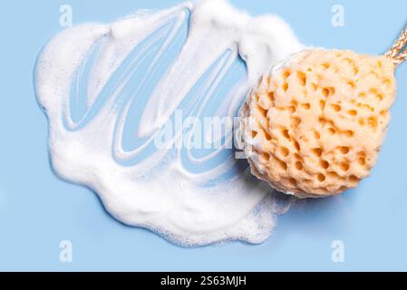 Face sponge with soap foam texture on blue background close up. Body care and hygiene concept. Stock Photo