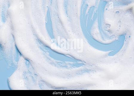 White soft foam texture swatch on blue pastel background. Face cleanser mousse sample, soap foam. Stock Photo