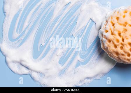 Sponge with white foam texture on blue background close up. Body care, dishware, cleaning and hygiene concept. Stock Photo