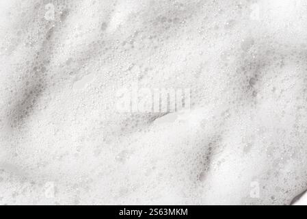 White fluffy foam as background. Face cleanser foam texture sample on white surface close up. Stock Photo