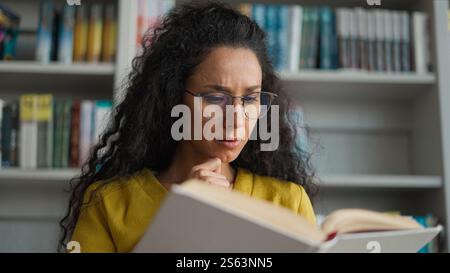 Indian Hispanic woman reader focused preparing exam reading book university library high school girl female student studying read learn textbook Stock Photo