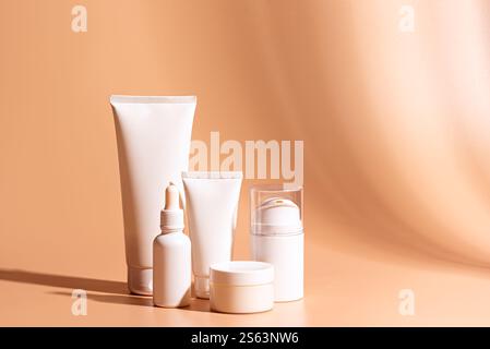 Cosmetic products containers on beige pink background with shadows, copy space. White blank face moisturizer cream jar, cleanser gel tube, face serum Stock Photo