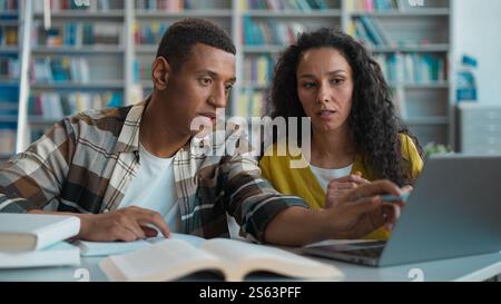 Students African American man Caucasian Hispanic woman teamwork project exam preparation laptop library university study computer e-learning Stock Photo