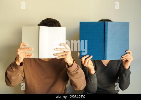 Young man and young woman holding books in front of their faces with both hands Stock Photo