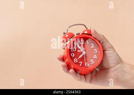 Red alarm clock in hand on beige background. Time concept Stock Photo