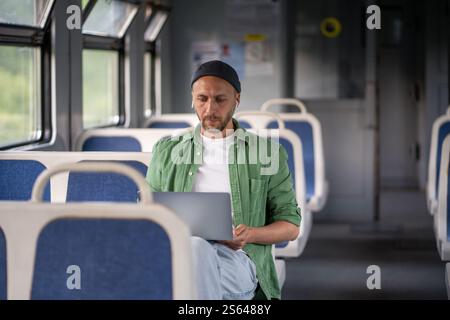 Focused thoughtful man passenger working on laptop while travel by electric train using earphones  Stock Photo