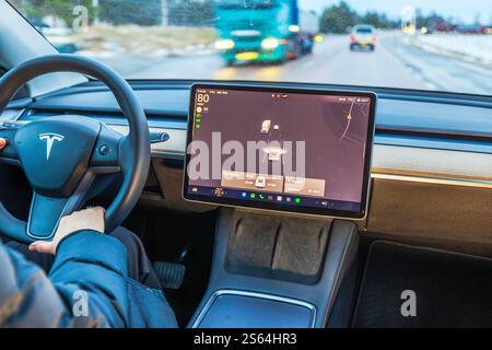 Woman driving Tesla Model Y on a winter road with touchscreen showing vehicle proximity and tire pressure. Sweden. Stock Photo