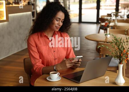 Woman using smartphone while working in cafe Stock Photo