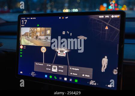 Tesla Model Y central screen displaying rear camera and surrounding traffic view when turn signal is activated in city at night. Sweden. Stock Photo