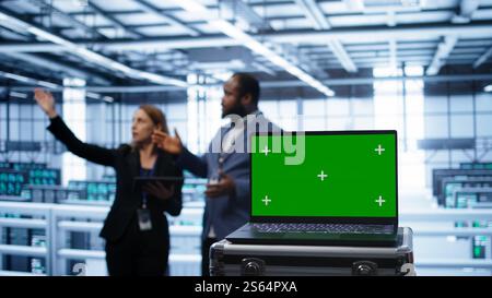 Green screen laptop used by engineers monitoring server room, doing checkup. Focus on chroma key notebook used by IT support employee working in data center facility, camera B close up Stock Photo