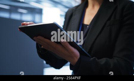 Programmer managing data center with advanced technology using digital device. Close up shot of woman walking in server room, optimizing data center tech with tablet, camera B Stock Photo