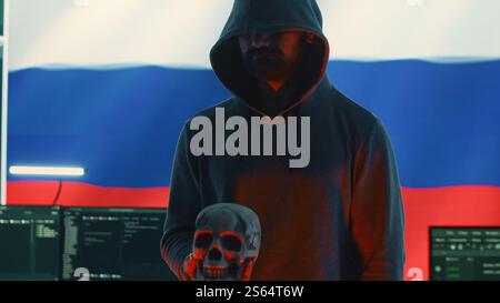 Russian cyber criminal making harmful death threats with a skull, conceptual image of cyberterrorism and cybercrime. A person with dark hood embodying terror and panic among the population. Camera A. Stock Photo