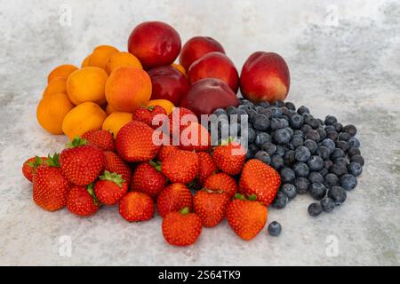 Freshly harvested summer fruits including ripe strawberries, blueberries, apricots, and nectarines arranged on a light marble surface Stock Photo