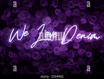 Pink neon sign "We Love Denim" in front of jeans background. Stock Photo