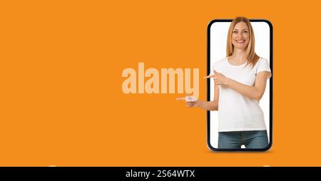 Person interacting with a smartphone against a vibrant orange background Stock Photo