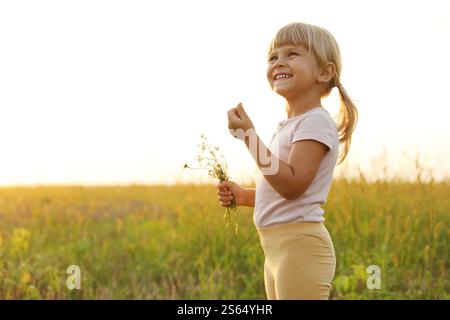 Cute little girl with chamomiles at meadow, space for text. Child enjoying beautiful nature Stock Photo