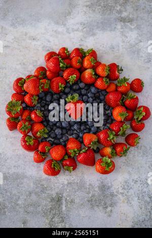 Vertical composition of fresh strawberries and blueberries arranged in a circular pattern on a rustic gray background Stock Photo