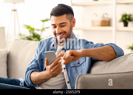 Smiling jew man using smart phone sitting on couch Stock Photo