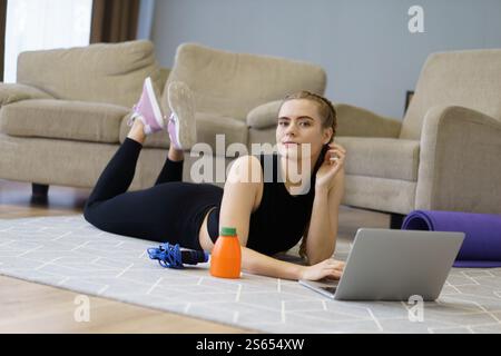 Woman is laying on the floor with a laptop and a bottle of orange juice. She is wearing pink shoes Stock Photo