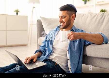 Smiling jewish man watching video on computer, drinking coffee Stock Photo