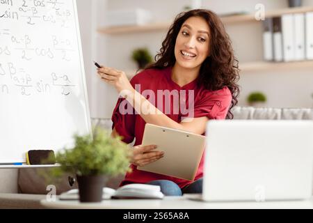 Lady teacher explaining math to students using laptop holding clipboard Stock Photo