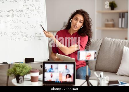 Lady teacher in earbuds explaining trigonometric functions to students online Stock Photo