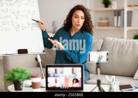 Lady teacher explaining math online showing clipboard to laptop Stock Photo
