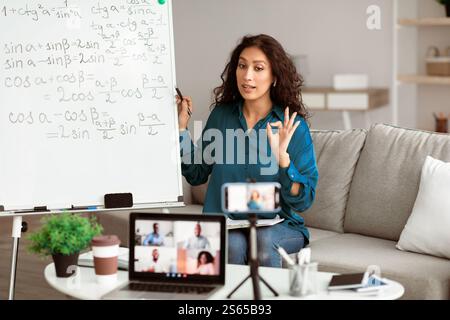 Lady teacher showing ok gesture, explaining math to students Stock Photo