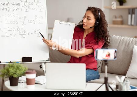 Lady teacher explaining math online showing clipboard to laptop Stock Photo