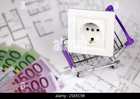 European standard EU outlet in small shopping cart on blueprints of residential house plan close up. Concept of shopping and electricity devices. Stock Photo
