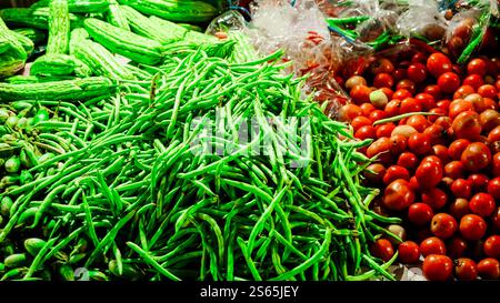 A vibrant display of fresh vegetables including green beans, bitter gourds, and cherry tomatoes at a market stall. Stock Photo