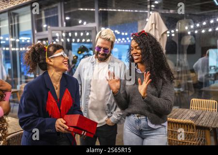 Happy woman receiving birthday gift during night party with friends in a bar Stock Photo
