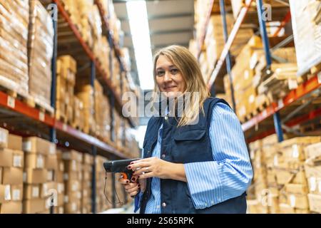 Portrait of a happy blonde female warehouse worker smiling at camera while standing doing inventory using scan reader Stock Photo